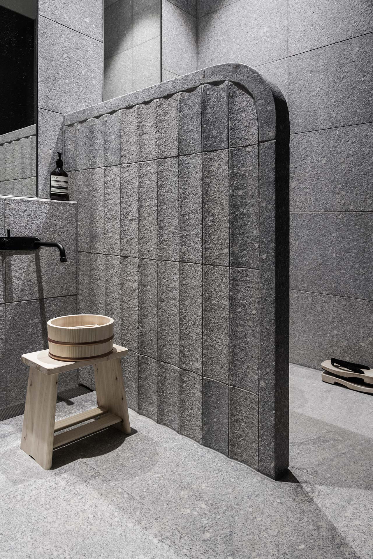 The bathroom is clad with stone tiles and reminds of Eastern spas