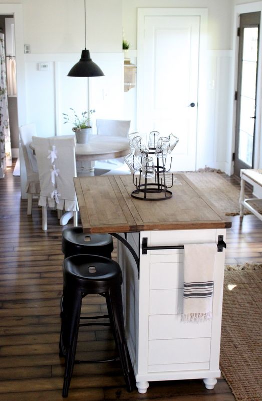 a mini kitchen island in white with a wooden tabletop and rails on each side can be used for breakfasts or having drinks