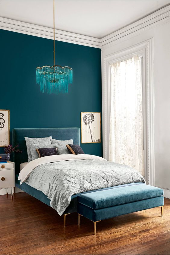 a bold teal wall for a statement and a dusty blue upholstered bed plus a matching ottoman