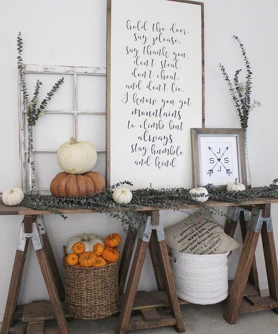 a farmhouse trestle table with dried eucalyptus, white and orange pumpkins, signs and baskets