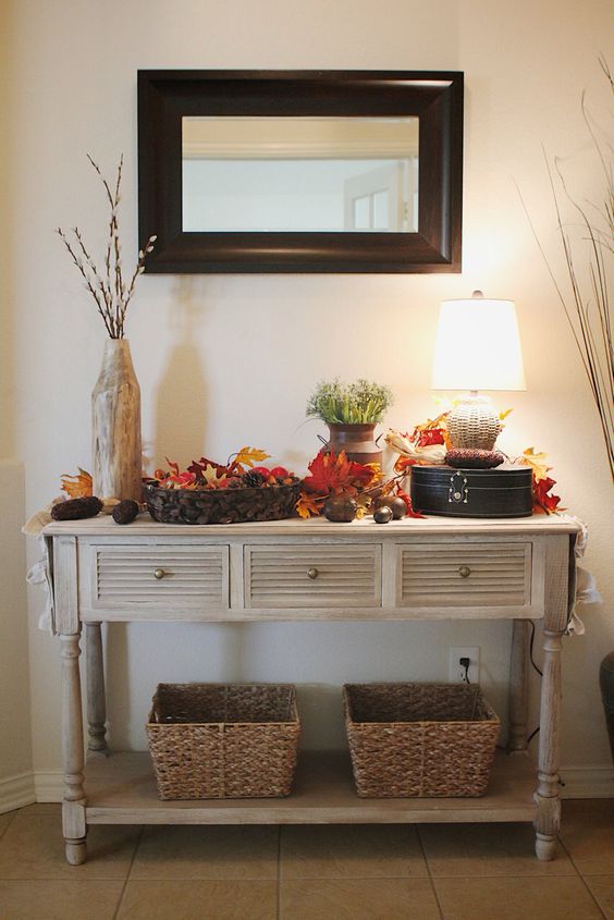 a vintage rustic console table with baskets, fall leaves, pinecones, corn cobs and greenery in a vase