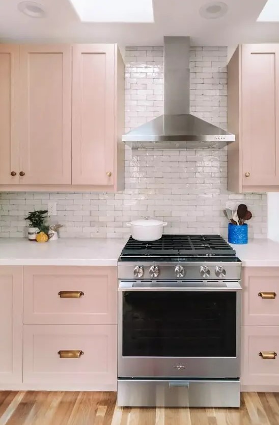 a beautiful blush kitchen with brass handles, a white tile backsplash and skylights is very tender and delicate