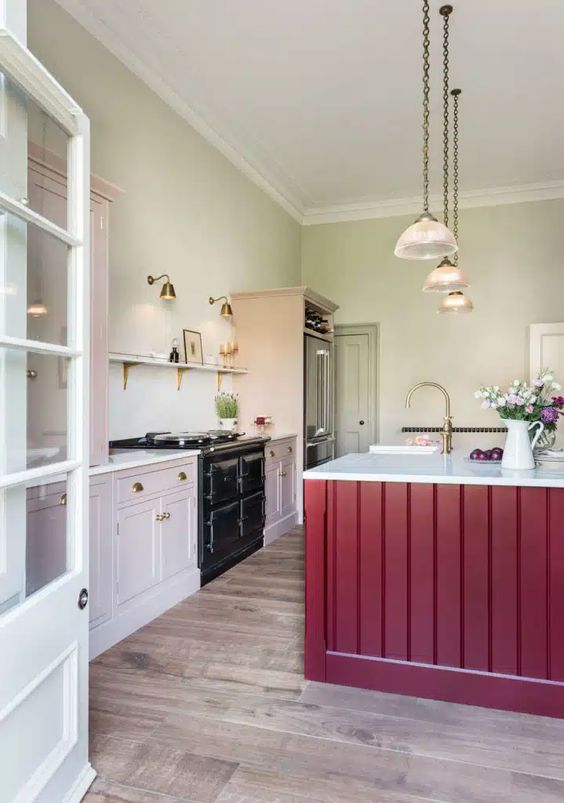 a beautiful kitchen with pale green walls and blush cabinets, white stone countertops and a shelf, a fuchsia kitchen island and pendant lamps
