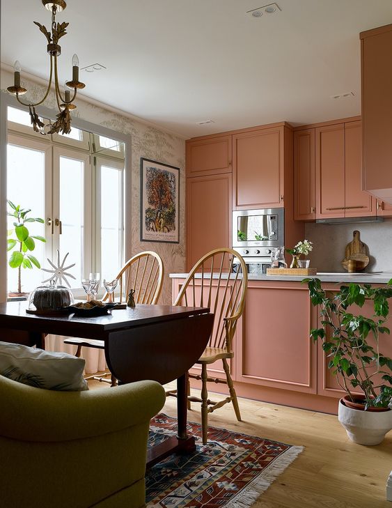 a beautiful peachy pink kitchen with a kitchen island and built-in appliances plus a dining zone with a folding table