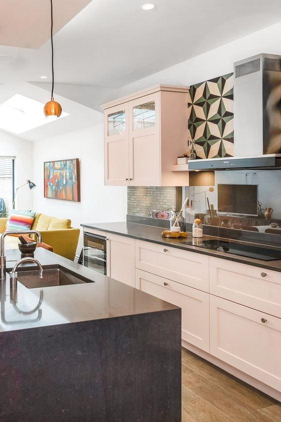 a blush kitchen with a black kitchen island, black countertops, a green kitchen backsplash and brass knobs