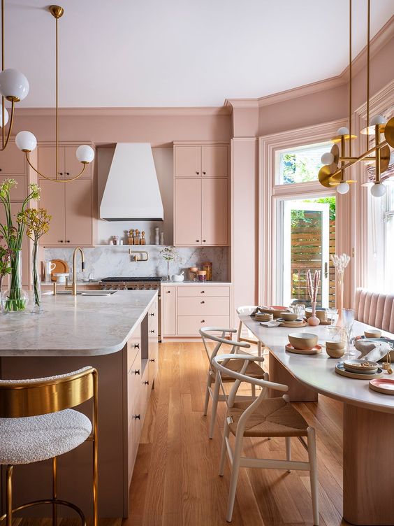 a blush kitchen with sleek cabinets, a large dining zone with a sofa, an oval table, a large kitchen island and gold touches