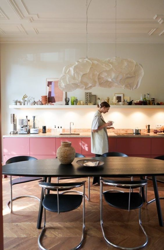 a bold pink kitchen with lower cabinets, a terrazzo countertop, a long shelf with decor and some built-in lights