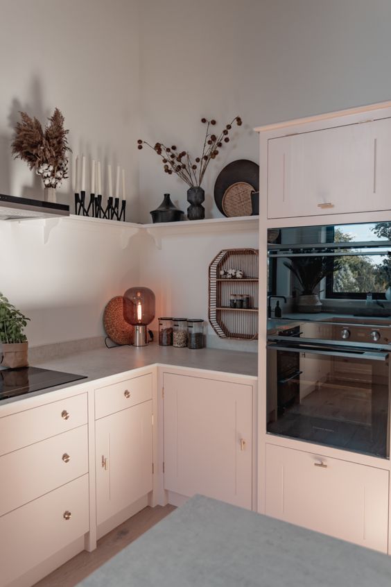 a chic blush kitchen with a grey stone countertop, a long shelf instead of upper ones and built-in appliances