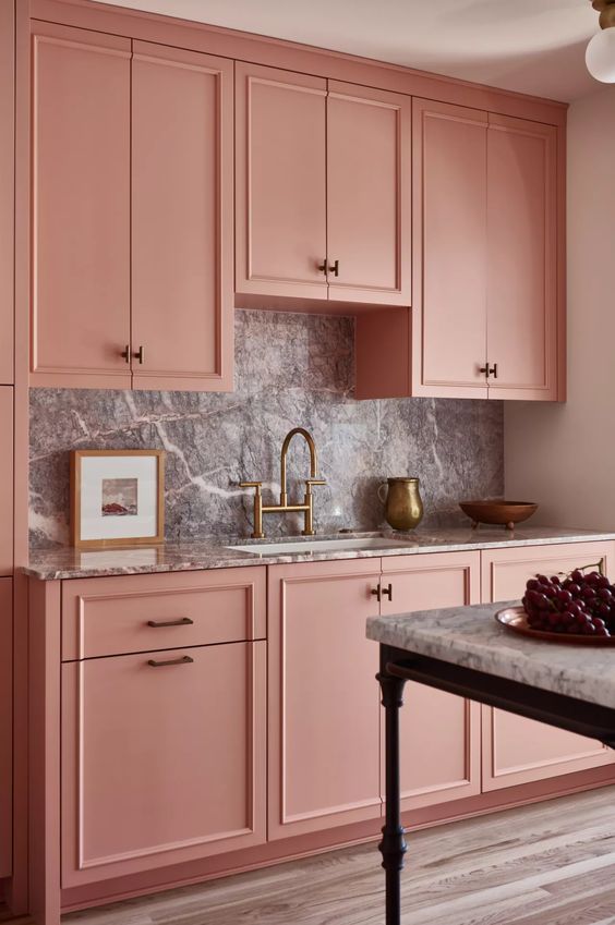 a chic pink kitchen with a grey stone backsplash and countertops, brass and gold touches and black is pure elegance