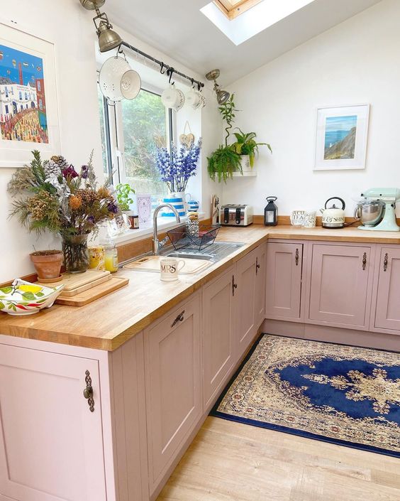 a dusty pink lower cabinet kitchen with butcherblock countertops, some decor and greenery and a skylight