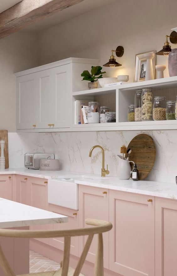 a lovely and welcoming kitchen with pink and white cabinets, open storage compartments and a white stone backsplash and countertops