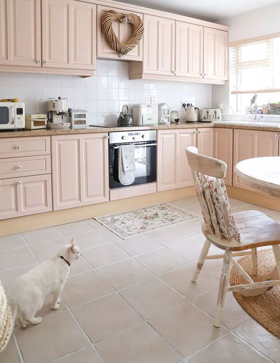 a lovely blush kitchen with shaker cabinets, stone countertops, a white square tile backsplash, a round table and shabby  chic chairs