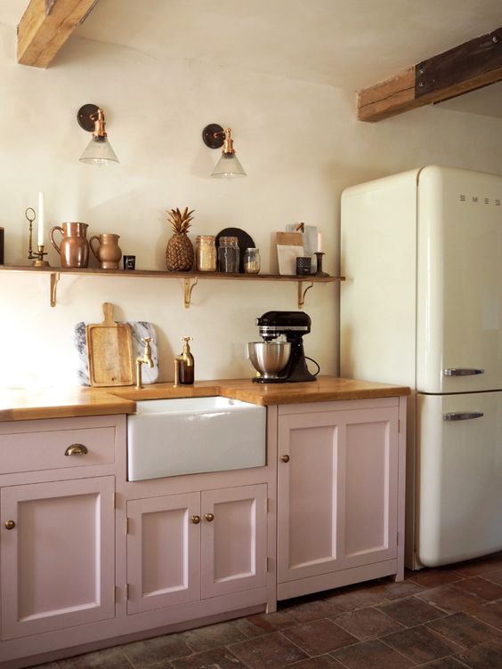 a neutral kitchen with light pink lower cabinets, a long shelf with decor, sconces, a neutral fridge is a lovely space