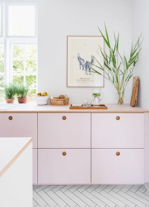 a pale pink kitchen with MDF cabinets, white stone countertops, potted herbs and lots of natural light