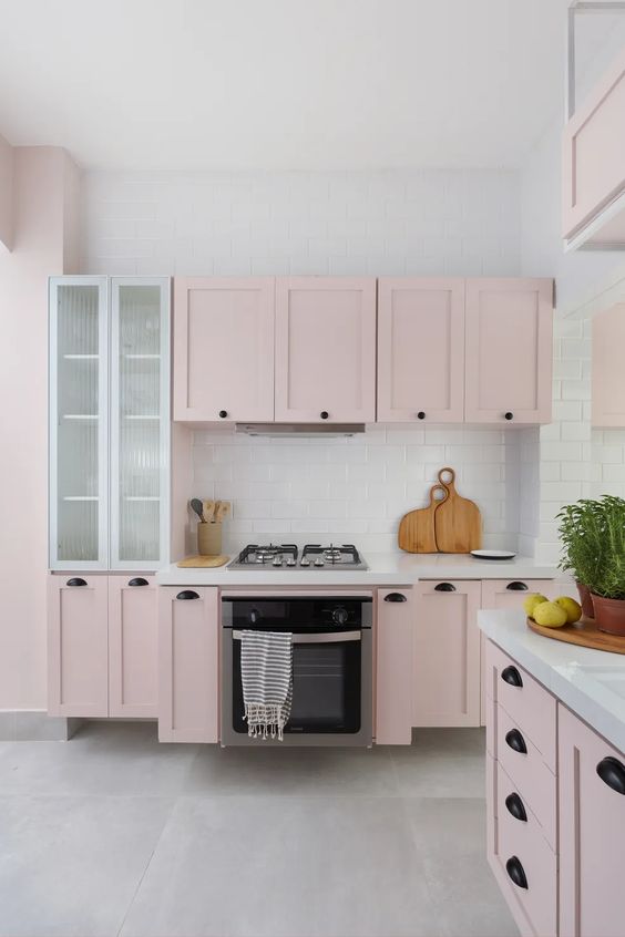 a pale pink kitchen with shaker cabinets, white stone countertops and a tile backsplash, black handles is amazing