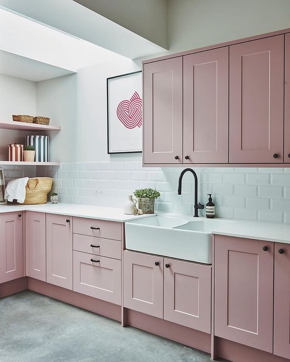a pale pink kitchen with shaker style cabinets, a white subway tile backsplash and white countertops, open shelves and a skylight