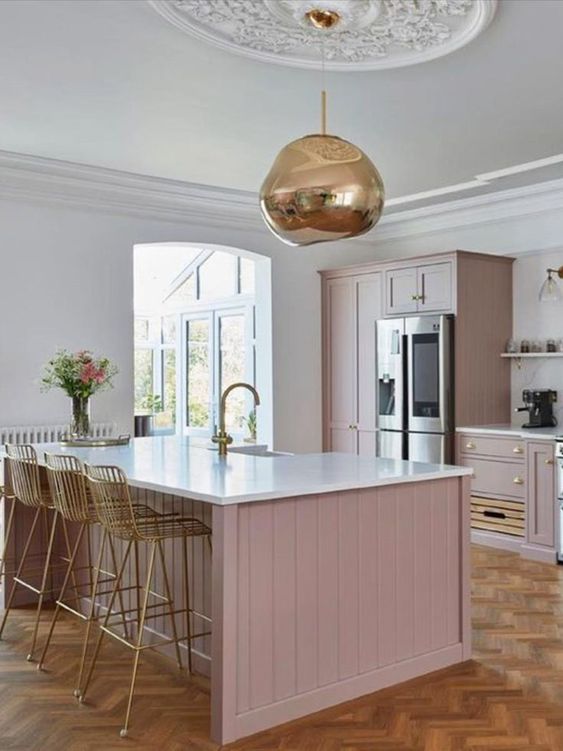 a pale pink kitchen with shiplap cabinets and white stone countertops plus a white stone backsplash, a gold pendant lamp and matching tall stools