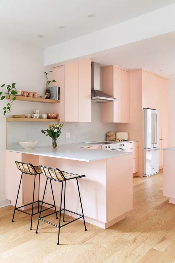 a peachy kitchen with sleek cabinets, a grey backsplash and countertops, blooms and greenery and tall stools