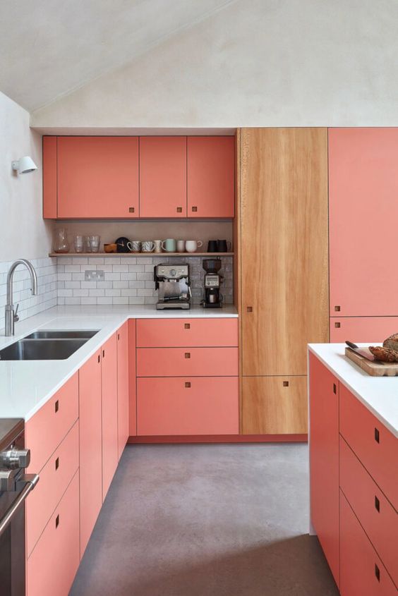 a pink kitchen with a white subway tile backsplash, a stained cabinet and no handles plus a shelf for storing decor