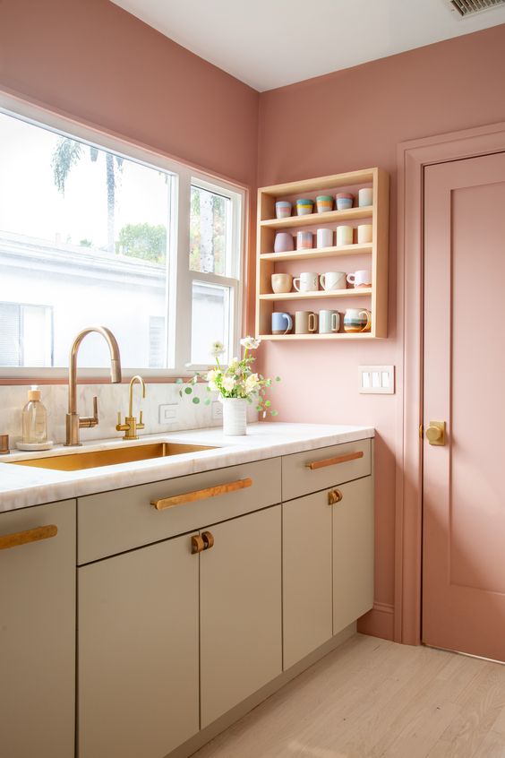 a pink kitchen with olive green cabinets, white stone countertops, an open shelf for mugs and cool handles and pulls