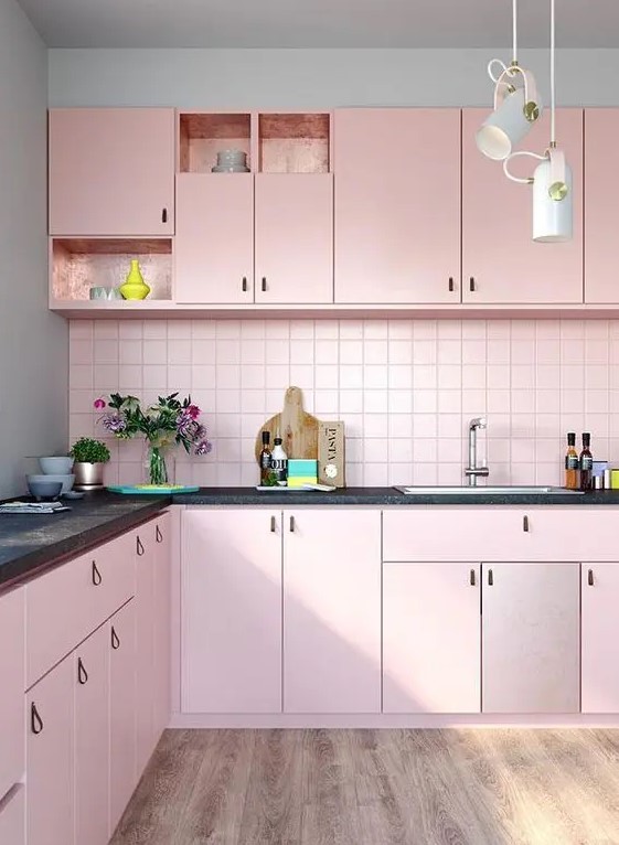 a pretty pastel pink kitchen with leather handles, a matching pink backsplash and black countertops