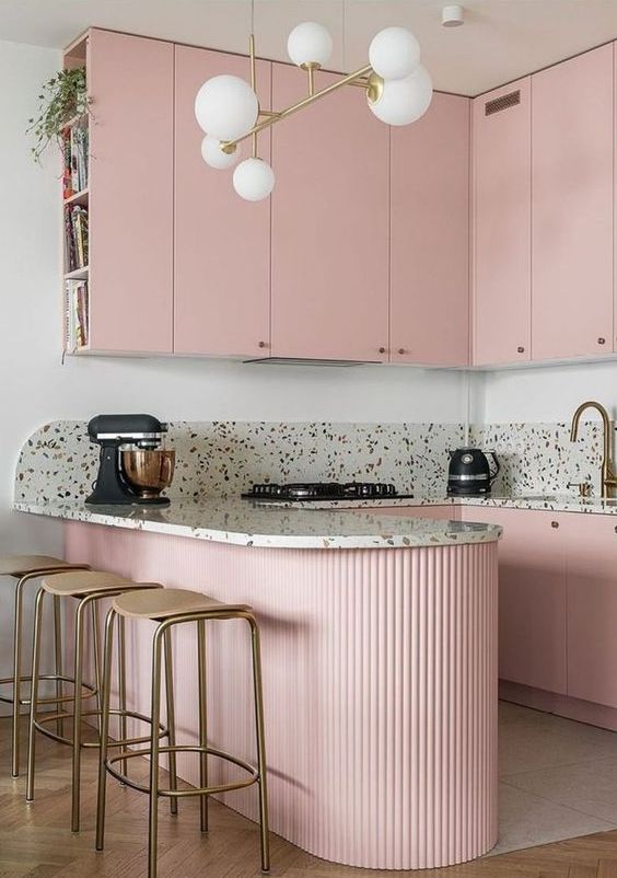 a pretty pink kitchen with sleek upper cabinets and a fluted kitchen island, terrazzo countertops and a backsplash, gold touches