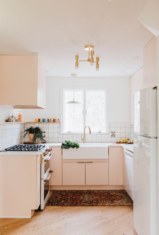 a small yet chic kitchen in blush and white, with a gold chandelier, a white tile backsplash and white countertops