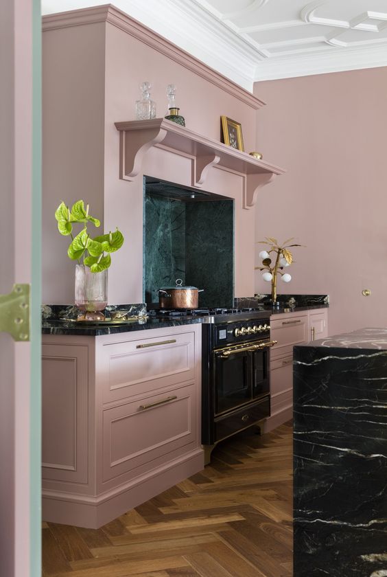 a sophisticated mauve kitchen with shaker cabients, a black marble kitchen island, built-in appliances and gold touches