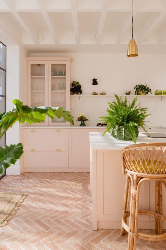 a welcoming pink kitchen with shaker cabinets, a large kitchen island, white stone countertops, a ledge with potted greenery and rattan stools