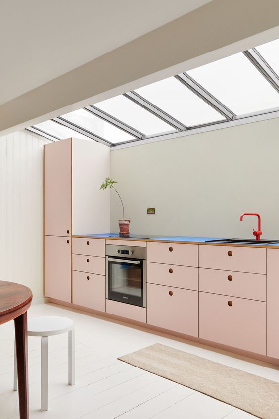 an attic kitchen with blush MDF cabinets, black countertops, a red faucet and lots of natural light is cool