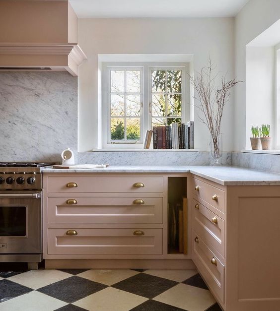 an elegant and chic kitchen done in blush, with white stone countertops and brass handles, a white stone backsplash and some potted plants