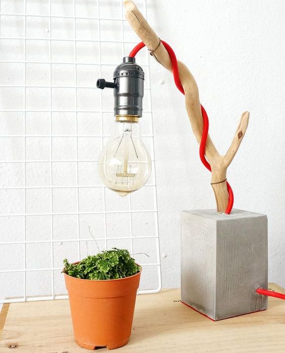 a creative table lamp of a concrete base, a branch and an industrial bulb on red cord is a contrasting piece
