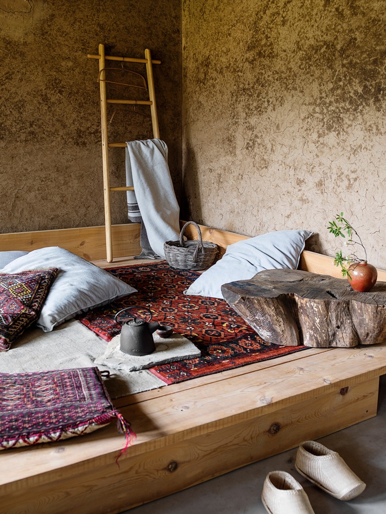 creative lounge area to relax during the day The lounge space is a wooden platform with pillows and rugs and a wooden stump table, look at the antique-looking walls