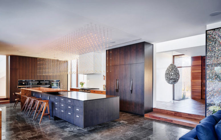 The kitchen is large, with sleek wooden cabinets and a giant kitchen island highlighted with amazing pendant light installation