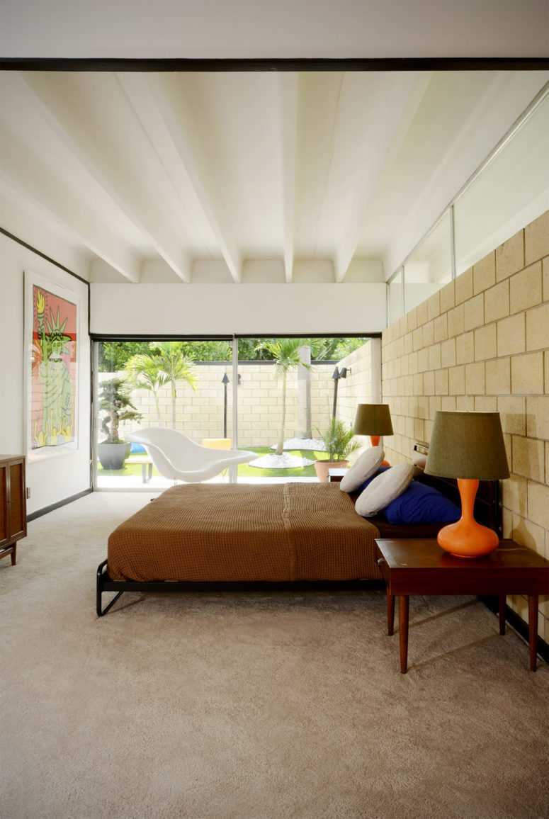 The master bedroom is opened up to outdoors with glass doors, there's colorful furniture and an artwork The master bedroom is opened up to outdoors with glass doors, there's colorful furniture and an artwork