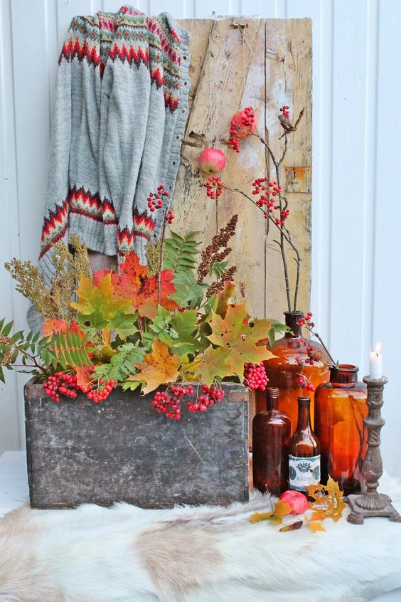 a stylish fall display with colorful bottles, candle holders, a concrete box with fall leaves and berries
