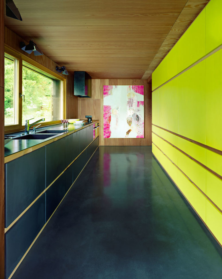 The kitchen is done in black with a contrasting neon yellow wall and a bold artwork