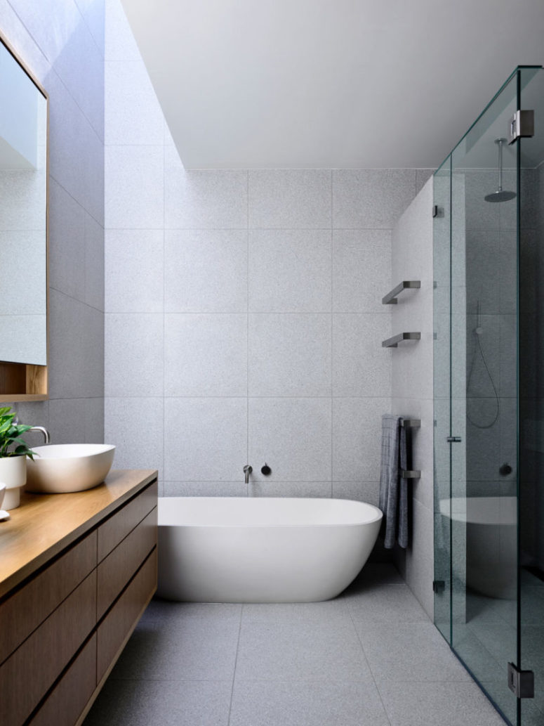 The bathroom is done with a wooden vanity, stone-inspired tiles and a glass door