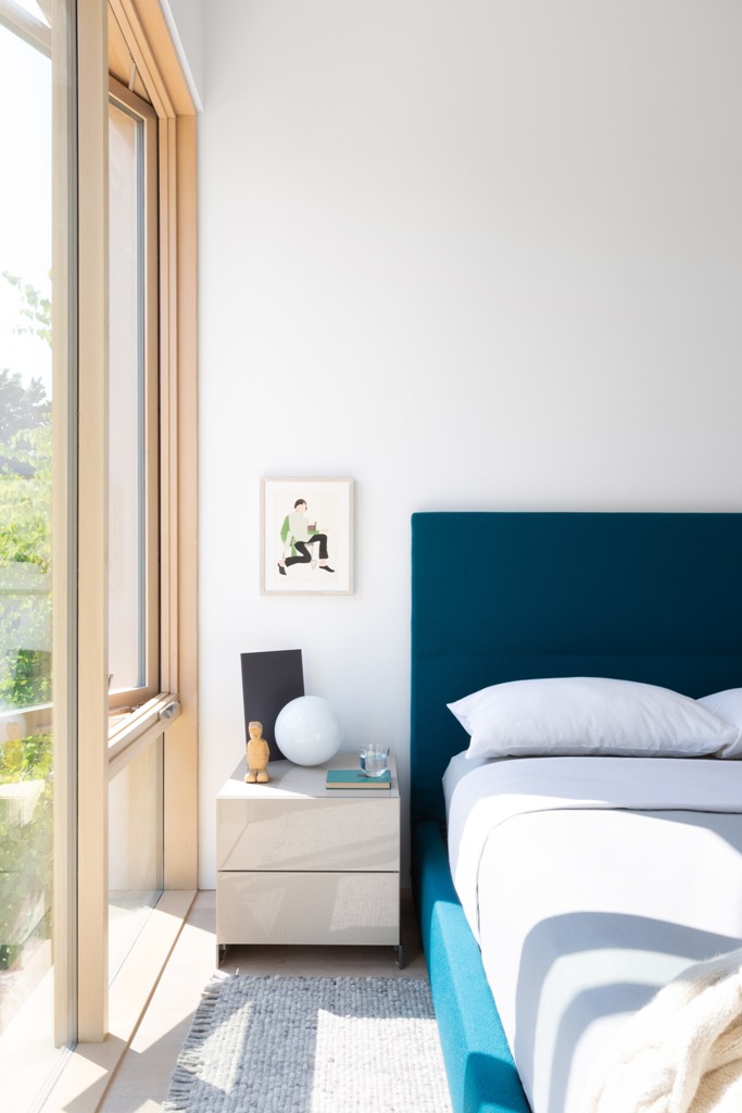 The master bedroom is done with a blue upholstered bed, it's filled with light thanks to extensive glazing The master bedroom is done with a blue upholstered bed, it's filled with light thanks to extensive glazing
