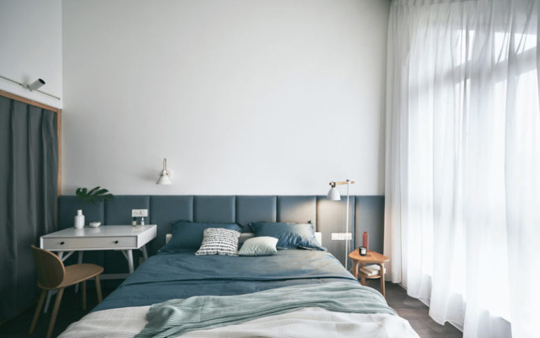 The master bedroom is a peaceful space in blue and white, with an upholstered headboard and a window that takes the whole wall