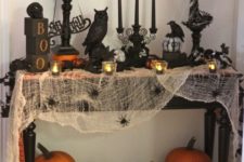 a Halloween console with spiderweb, fresh pumpkins, black candles and various figurines for a spooky feel