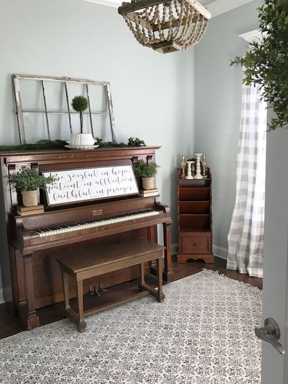 a rustic piano and a stool, an evergreen runner, potted greenery and an artwork placed on the piano