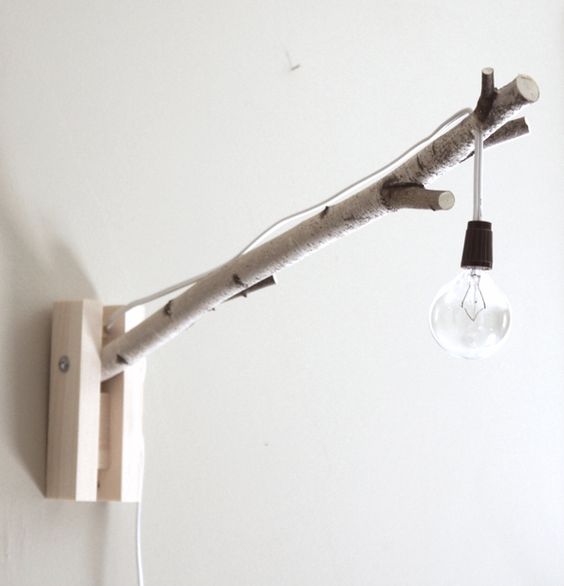a simle natural and industrial wall lamp with a birch branch and a simple bulb on cord
