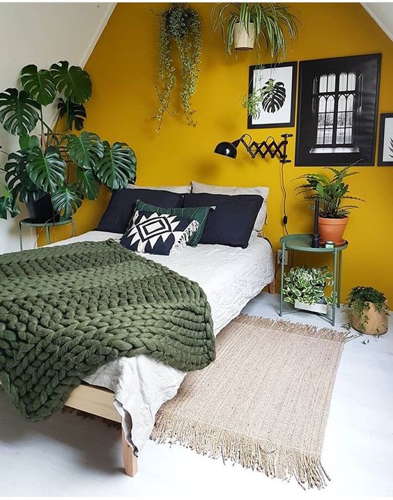 a mustard accent wall and touches of dark green and potted plants make up a bold boho space
