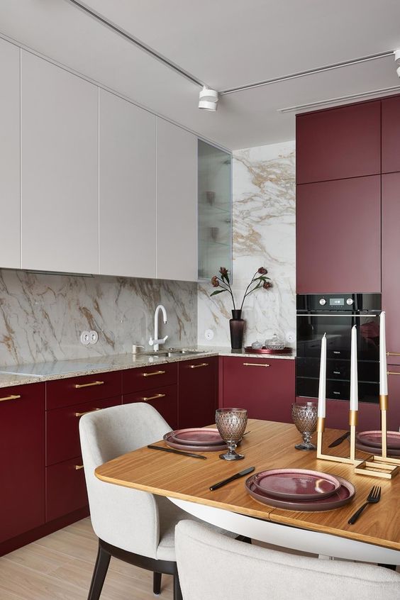 a beautiful burgundy and white eat-in kitchen with white stone countertops, a table and neutral chairs and built-in appliances