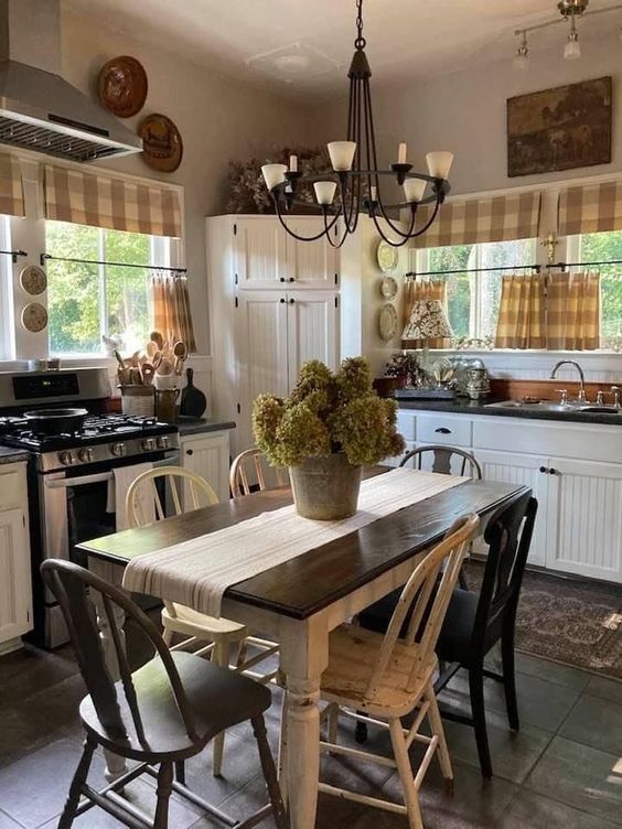 a farmhouse kitchen with planked cabinets, black countertops, a table and mismatching chairs, a chandelier and plaid textiles