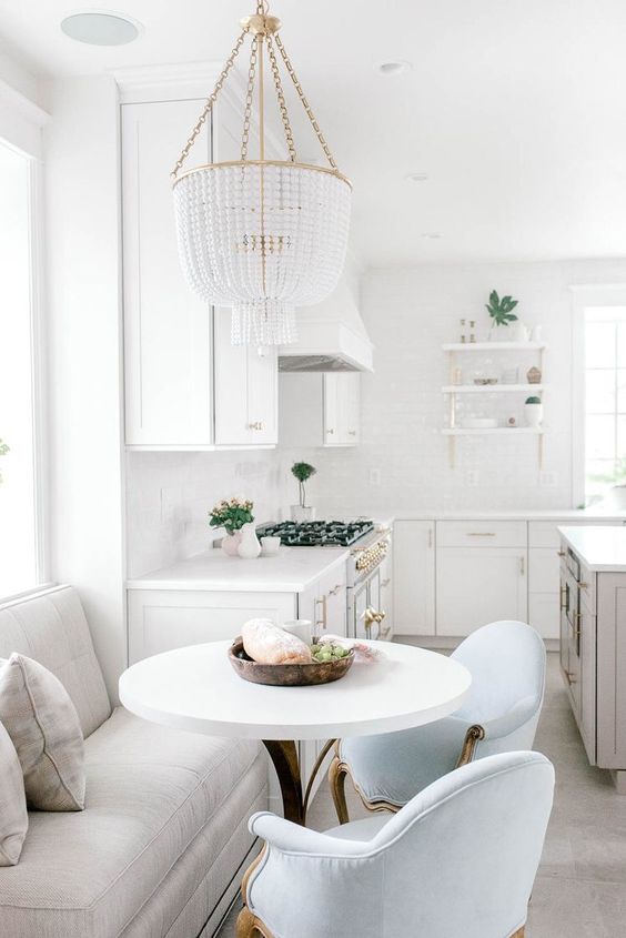 a glam white farmhouse kitchen with a grey kitchen island and a dining zone with a loveseat and blue chairs