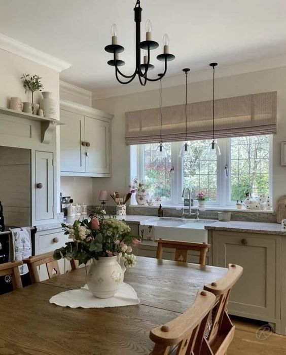 a grey farmhouse kitchen with shaker cabinets, a stained dining set, lamps and a chandelier and some plants and blooms