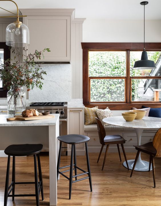 a pretty greige modern farmhouse kitchen with a kitchen island and a dining zone with a windowsill bench and a table in the corner