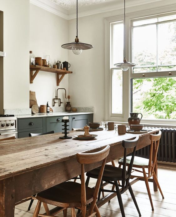 a pretty rustic meets Scandinavian kitchen with dark green cabinets, a stained dining set with matching chairs and pendant lamps